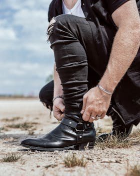 Close-up of a man adjusting his black leather boots outdoors, showcasing modern fashion.